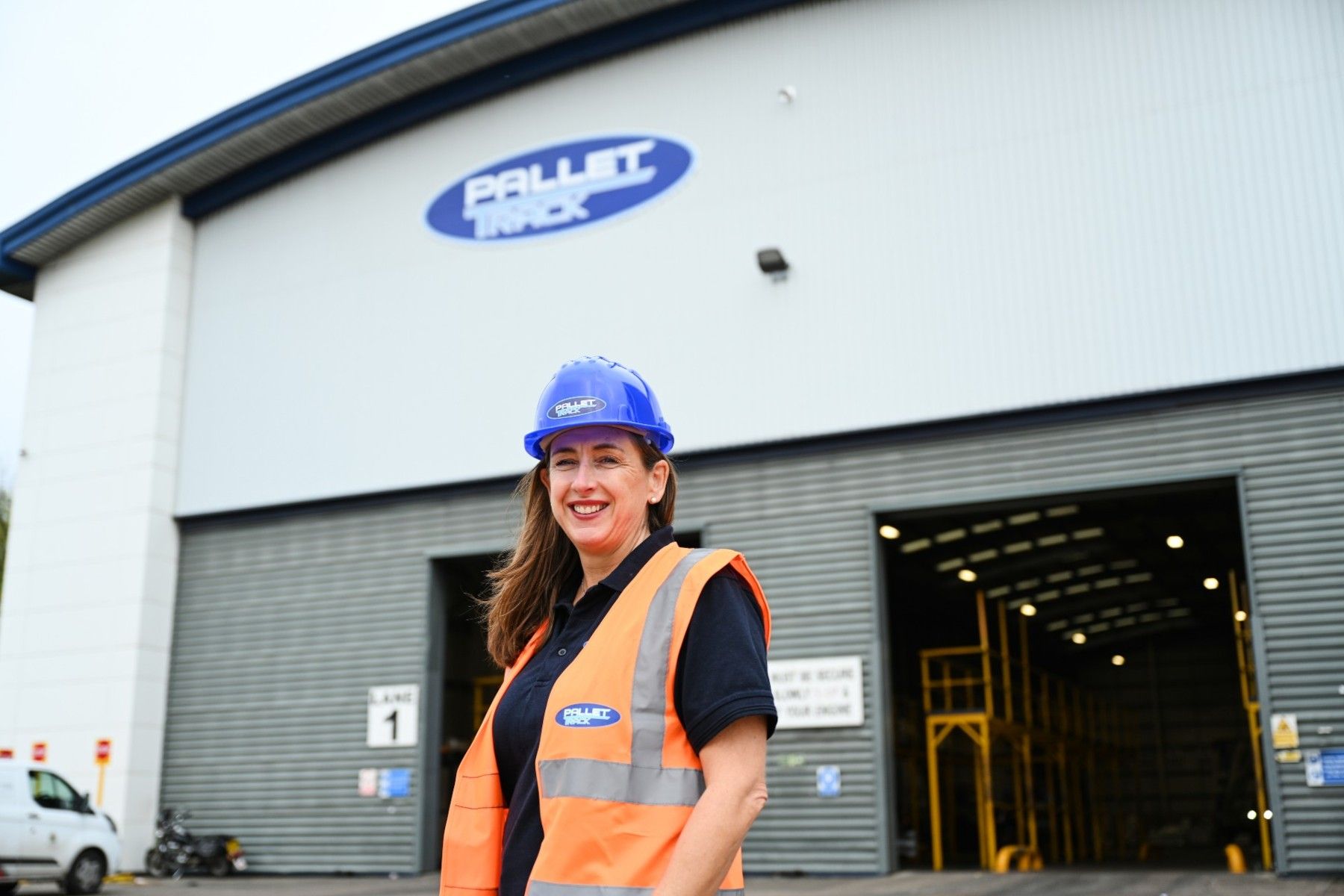 Caroline Green in Hi Viz Standing in front of Pallet Track Warehouse